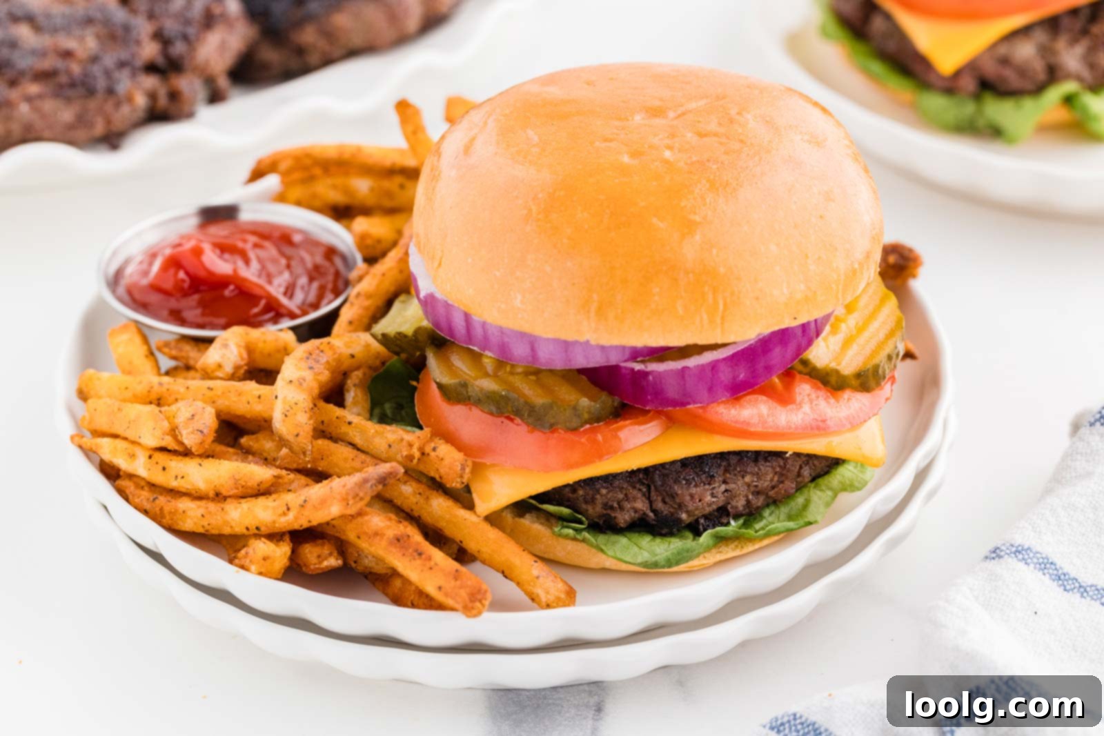 Two venison burgers on white plates, served with a side of crispy golden fries, ready to eat