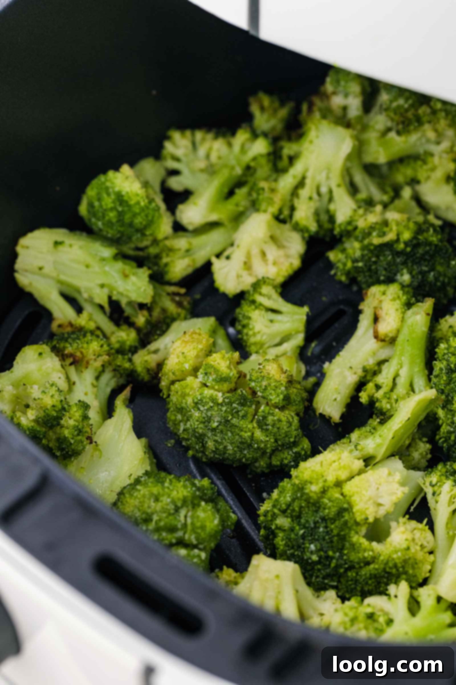 Air fryer frozen broccoli florets are seasoned and cooked in an air fryer basket, resulting in roasted pieces with a slightly crisp texture.