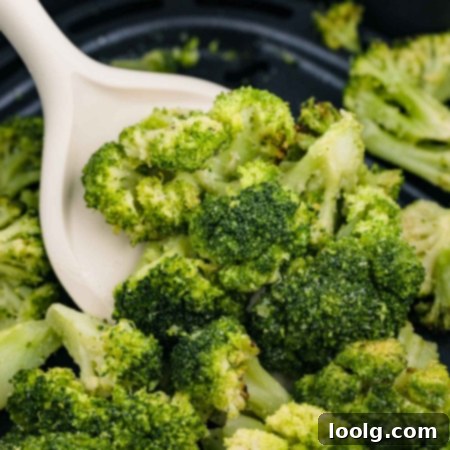 A white spoon lifts air fryer frozen broccoli florets from a black surface, showing their vibrant green color and slightly crisp texture.