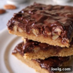 closeup image of decadent turtle cookie bars stacked on a plate, showing the chocolate, caramel, and pecan layers