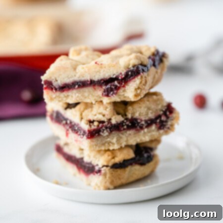 Ruby Red Cranberry Shortbread Gems 4 Image of a stack of rich, buttery cranberry shortbread bars filled with tart cranberry sauce on a white plate