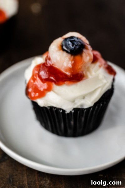 Ghoulish Gaze Cupcakes 3 Close-up of a lychee eyeball with a blueberry pupil and strawberry jam 'blood' on a cupcake.