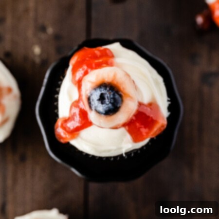 Ghoulish Gaze Cupcakes 7 top view photo of Eyeball Cupcakes for Halloween that have a moist chocolate base, cream cheese frosting and eyeballs that consist of canned lychees, and blueberries and strawberry jam to look like “blood” dripping down the frosting.