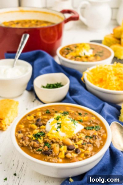 Nutritious Fiesta Soup 2 A large, steaming bowl of healthy taco soup, garnished with sour cream, cheese, and fresh cilantro, is presented on a rustic wooden table with additional toppings in the background. The soup is rich in color with visible beans, corn, and ground beef, promising a hearty and flavorful meal perfect for cooler weather.