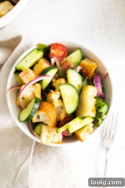 Rustic Tuscan Bread Salad 2 A bowl of vibrant Panzanella salad, featuring toasted bread cubes, ripe red tomatoes, green arugula, and sliced cucumbers.