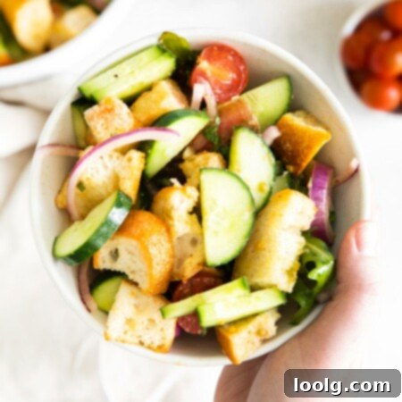 Rustic Tuscan Bread Salad 8 Photo showing a bowl full of green Tuscan-style panzanella salad loaded with chunks of bread, fresh ripe tomatoes, spicy arugula, crunchy cucumbers, sweet red onions, and zesty capers.
