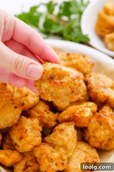 Crispy Air Fryer Popcorn Chicken 7 hand picking up a piece of golden brown popcorn chicken from the air fryer basket