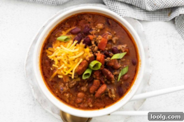 Venison Chili, Your Way: Slow Cooker or Stovetop 7 An overhead shot of a table laden with several bowls of venison chili, each garnished differently. One bowl features cheese and sour cream, another has fresh herbs, and a third might have avocado. There are also whole corn on the cob, slices of rustic bread, and a pitcher of drinks, setting a scene for a cozy meal.