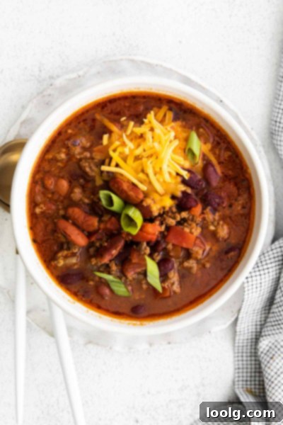Venison Chili, Your Way: Slow Cooker or Stovetop 9 A bowl of rich venison chili, garnished with a swirl of sour cream and a sprinkle of chopped green onions. The chili is in a white ceramic bowl, which is held by a person whose hands are visible, conveying a sense of comfort and home-cooked goodness. The background is subtly blurred, keeping the focus on the inviting meal.