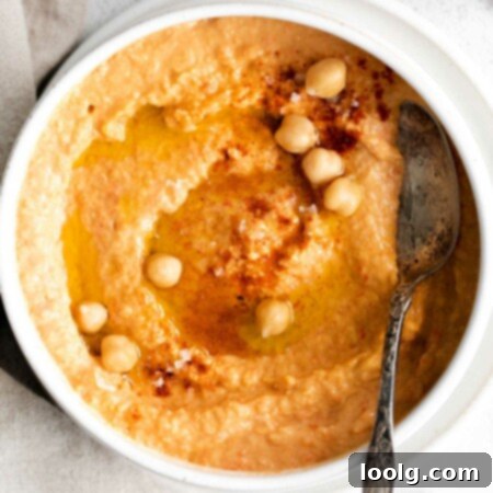 Smoky Red Pepper Hummus 8 close up image of roasted red pepper hummus with a few whole chickpeas and a dusting of paprika with a spoon set in the bowl