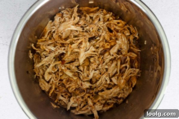 Effortless Instant Pot Shredded Chicken Tacos 7 Three shredded chicken tacos with various toppings arranged on a wooden board. A hand is reaching for one.