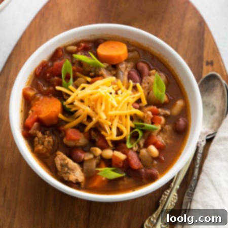 The Ultimate Instant Pot Turkey Chili 5 image of a wooden cutting board with a bowl of instant pot turkey chili topped with grated cheddar cheese and a silver spoon to the side