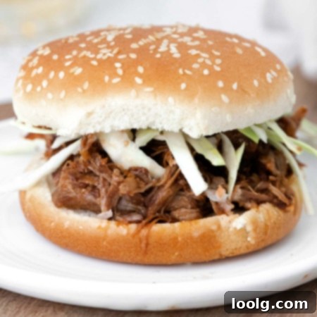 Fall-Apart Instant Pot Pork Shoulder 9 image of an instant pot pork shoulder sandwich showing perfectly seasoned pork shoulder on a hamburger bun garnished with raw cut green cabbage on a white plate