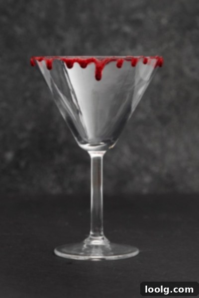 Crimson Kiss 4 A closer view of the Vampire's Kiss cocktail, showcasing the beautiful deep red color of the drink and the artistic 'bloody' rim. The cocktail is in a martini glass, ready for a Halloween celebration.
