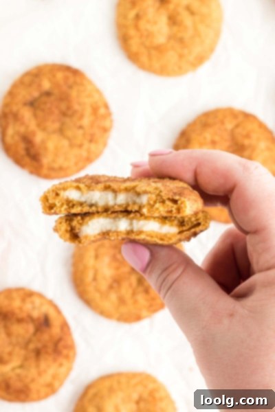 Pumpkin Cheesecake Delights 2 Two soft pumpkin cheesecake cookies on parchment paper, with a bite taken out of one to reveal the creamy cheesecake filling inside.