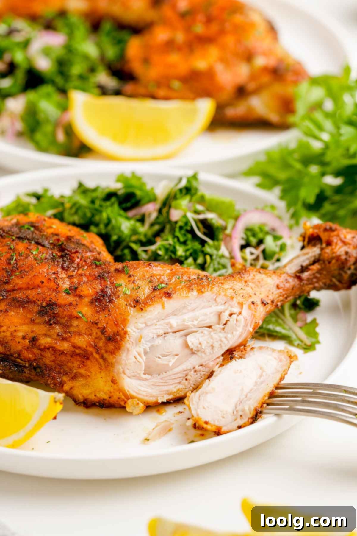 A plate of perfectly cooked, golden-brown air fryer chicken quarters, with a fork cutting into a juicy piece of chicken, alongside a fresh kale salad and lemon wedge.