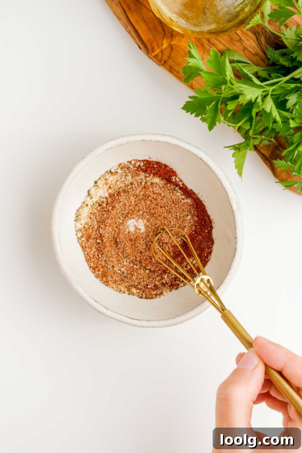 Process photo step one showing a white bowl of seasonings for air fryer chicken quarters, with a hand holding a golden whisk stirring the spices, and green parsley in the background.
