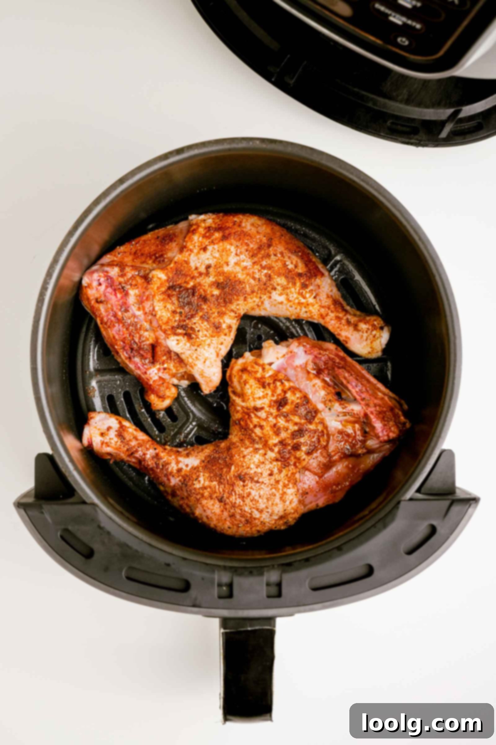 Seasoned chicken quarters perfectly arranged, skin-side down, in an air fryer basket, ready for cooking.