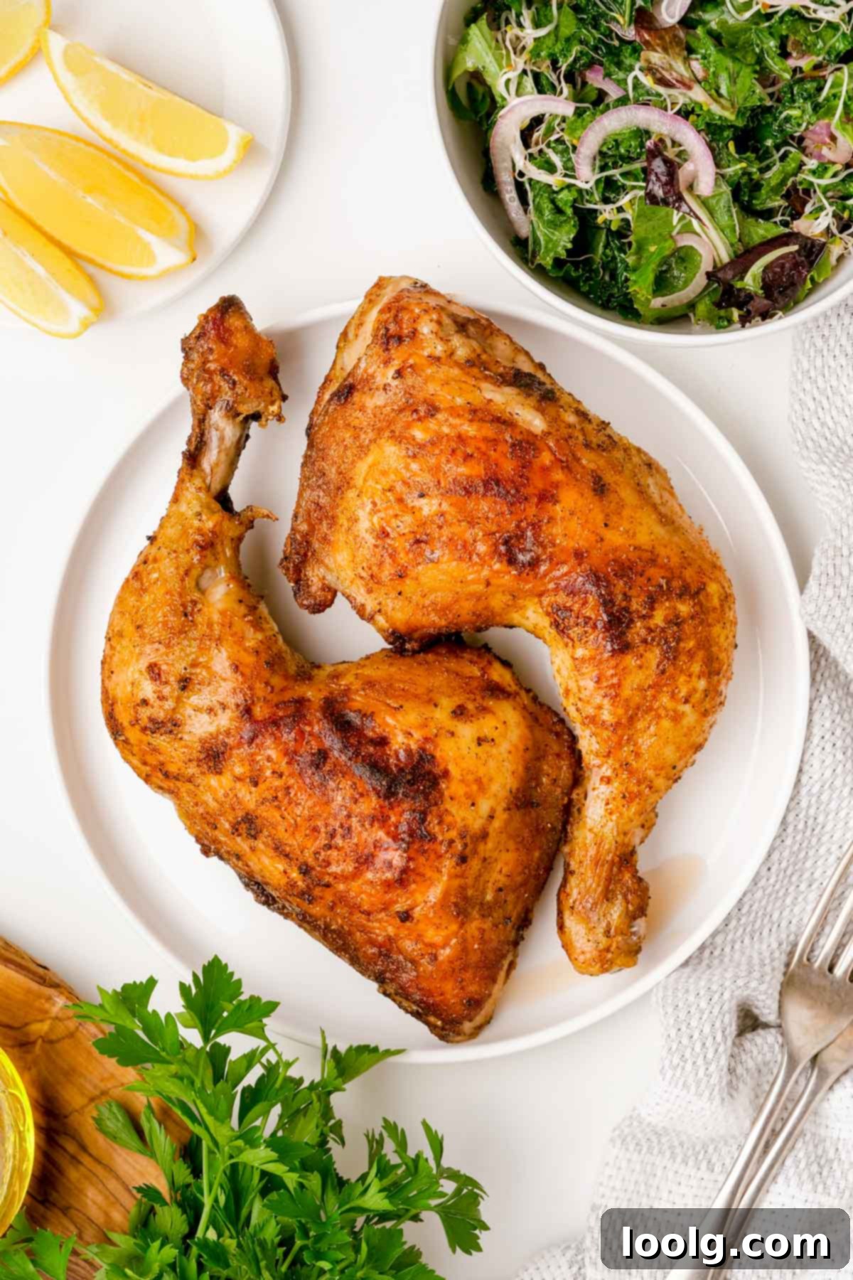 A beautifully plated air fryer chicken quarter on a white plate, garnished with fresh lemon wedges, a vibrant green salad, and fresh parsley in the background.