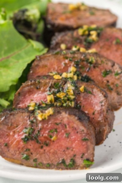 Prime Venison Loin 6 Sliced venison backstrap, perfectly cooked to medium-rare, reveals a juicy pink interior, garnished with fresh parsley and garlic butter.