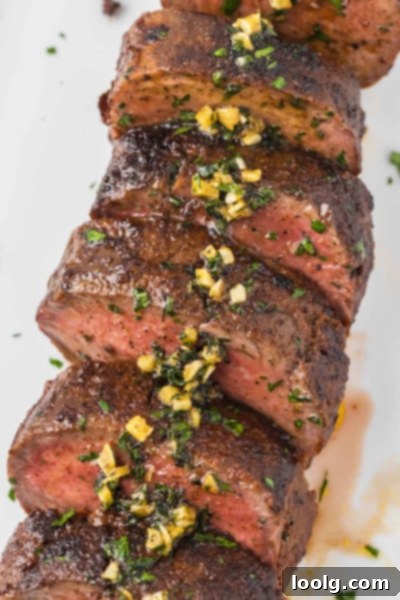 Prime Venison Loin 8 Close-up of the finished venison backstrap, sliced into medallions, topped with a generous spoon of rich garlic herb butter sauce and garnished with fresh parsley.