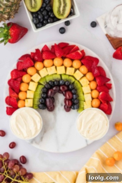 Kaleidoscope of Fruit 2 A vibrant rainbow fruit platter artfully arranged on a white marble lazy susan, featuring various colorful fruits with two small bowls of cream cheese dip at each end, resembling clouds.