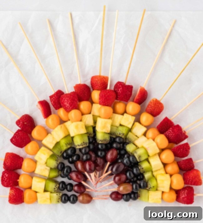 Rainbow Fruit Pops 3 Close-up of a single rainbow fruit skewer held against a bright background, showcasing the vibrant colors of each fruit.