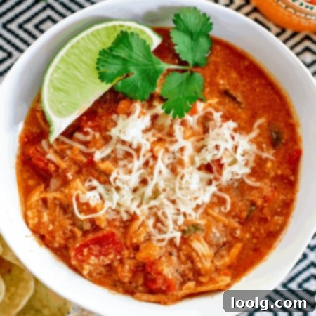 Qdoba's Signature Tortilla Soup 5 Overhead photo looking down on white bowl filled with Qdoba tortilla soup topped with shredded white cheese and garnished with a lime wedge and green parsley.