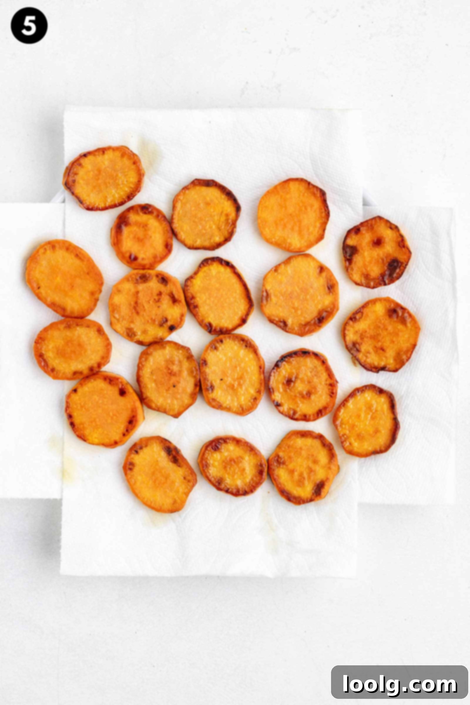Golden Crispy Fried Sweet Potatoes 5 fried sweet potatoes are arranged in a single layer on two overlapping white paper towels, displayed on a light-colored surface.