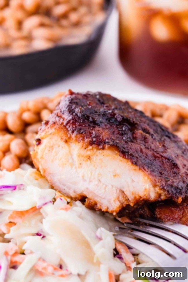 barbequed chicken thighs, cut into, on a white plate with baked beans and coleslaw