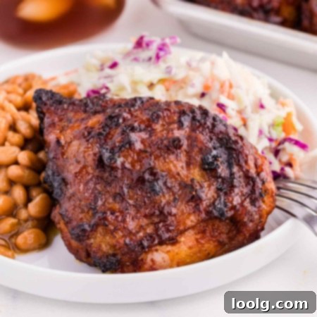 barbequed chicken thighs on a white plate with baked beans and coleslaw and a fork on the plate