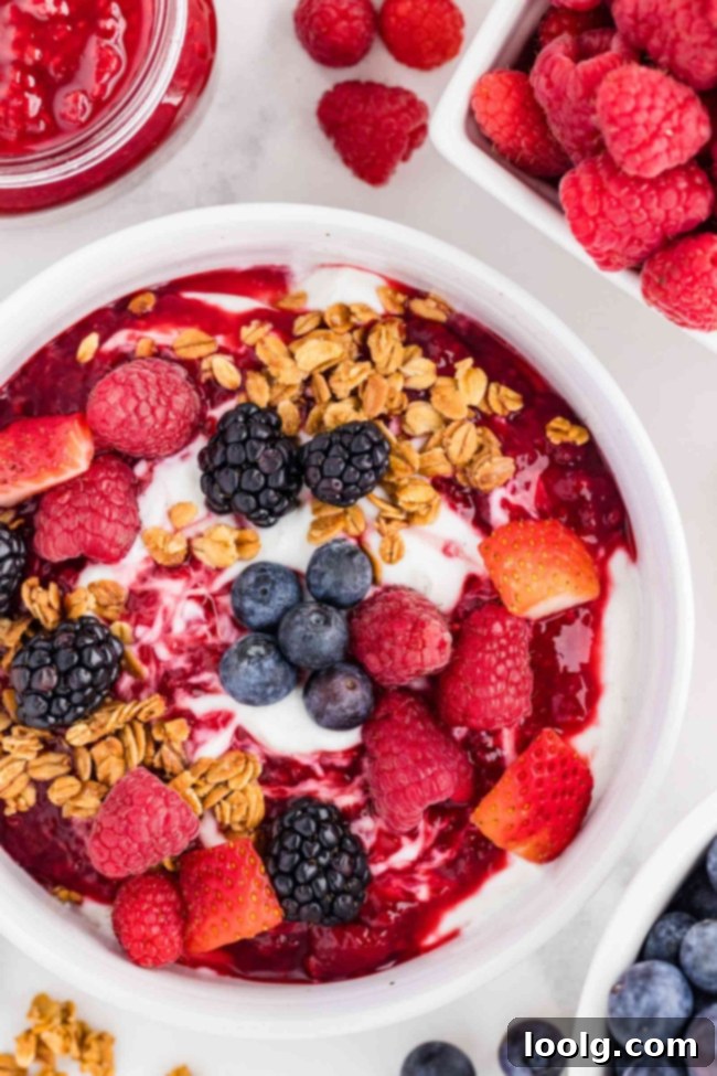 Delicious yogurt bowl with fresh berries and crunchy granola topped with raspberry compote in the background