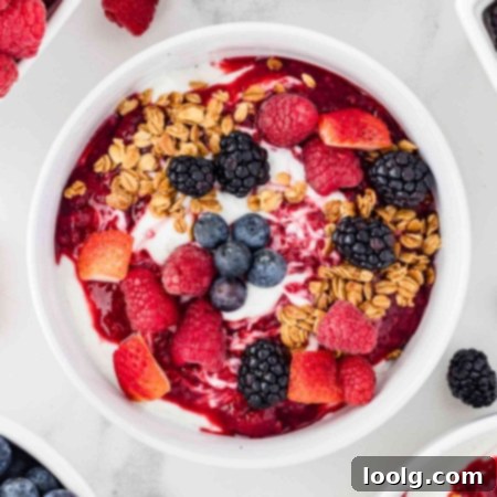 Overhead shot of yogurt bowls with berries and granola on top with more berries in the background