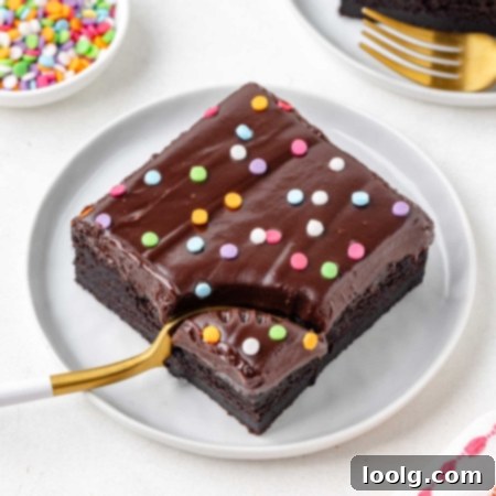 fork digging into a slice of a brownie with ganache on top on a white plate