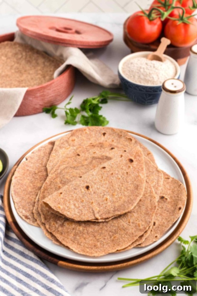 Homemade whole wheat tortillas stacked on a white plate with a tortilla warmer in the background, showcasing their freshness and appeal