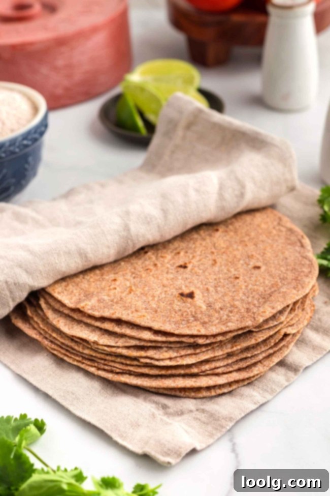 Freshly cooked whole wheat tortillas wrapped in a beige cloth on a white table, highlighting their warm and inviting appearance