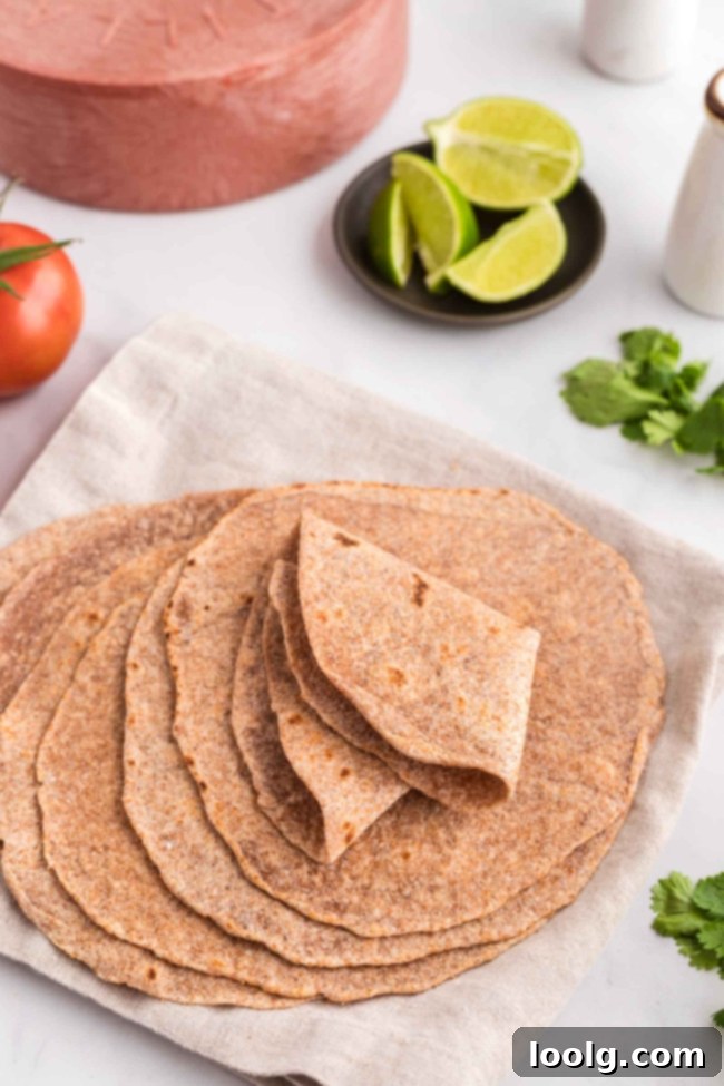 A stack of perfectly folded whole wheat tortillas on a white table, emphasizing their pliability and ease of use