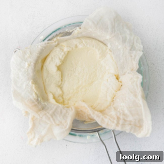 Fresh ricotta being strained using a cheesecloth in a sieve over a bowl
