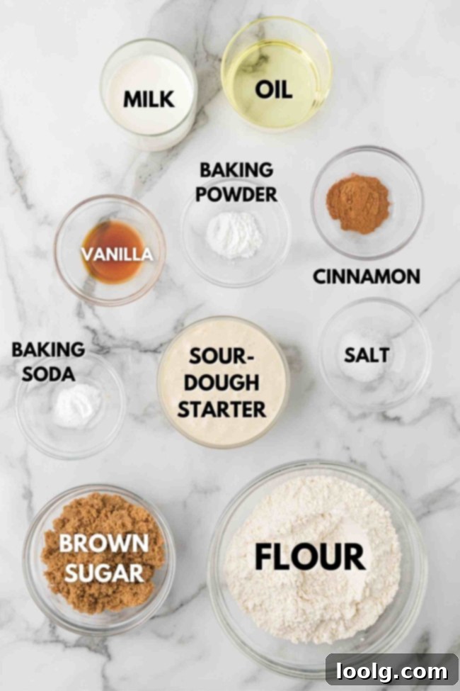 Ingredients for sourdough cinnamon muffins, including flour, sugar, milk, oil, and sourdough starter, arranged on a white surface.