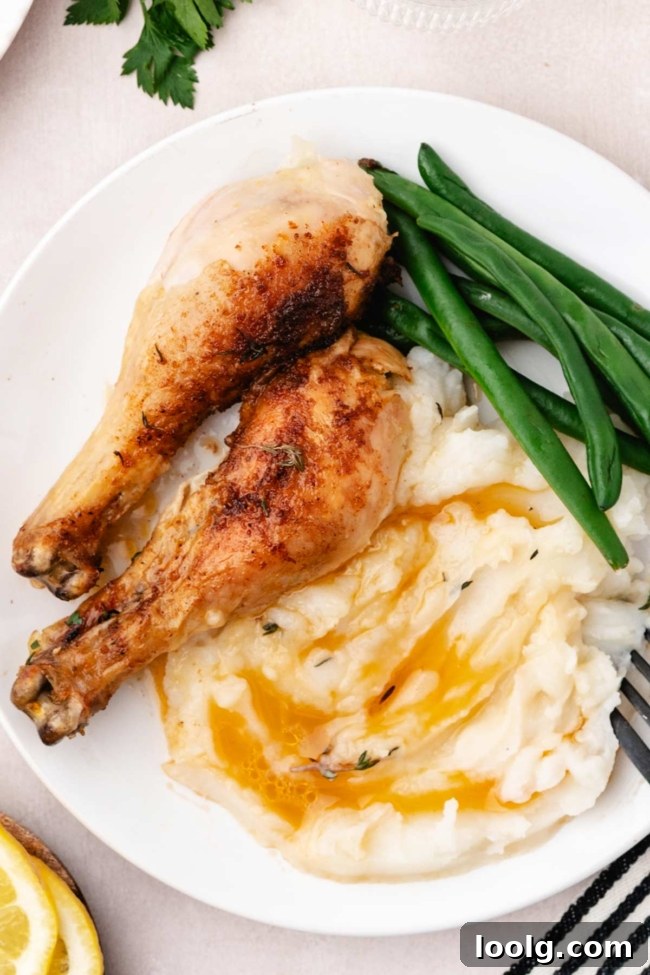 pieces of chicken on a white plate with mashed potatoes and green beans