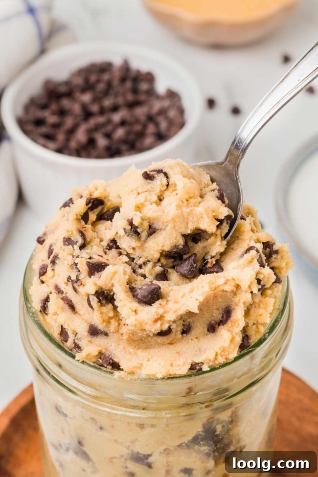 spoon digging into jar with cottage cheese cookie dough on a white table with bowl of chocolate chips in background