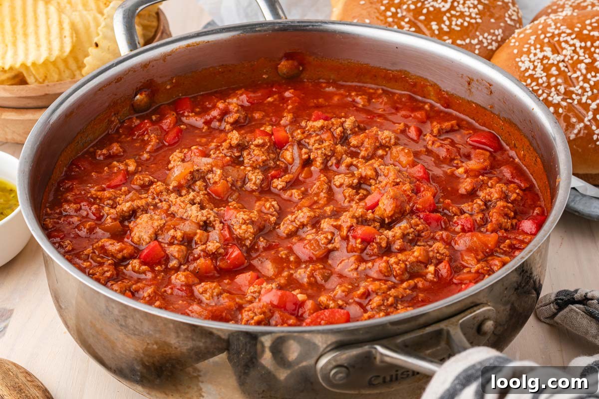 ground turkey sloppy joe filling in a skillet with sandwiches and chips in the background