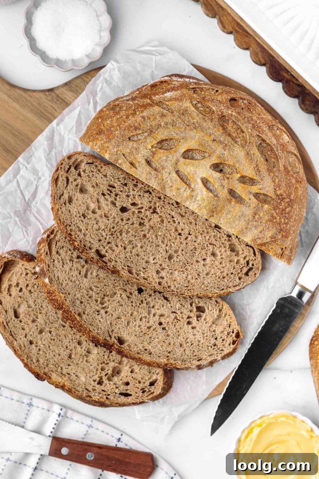 Whole wheat sourdough bread loaves and slices displayed on a wooden board with a knife and butter.