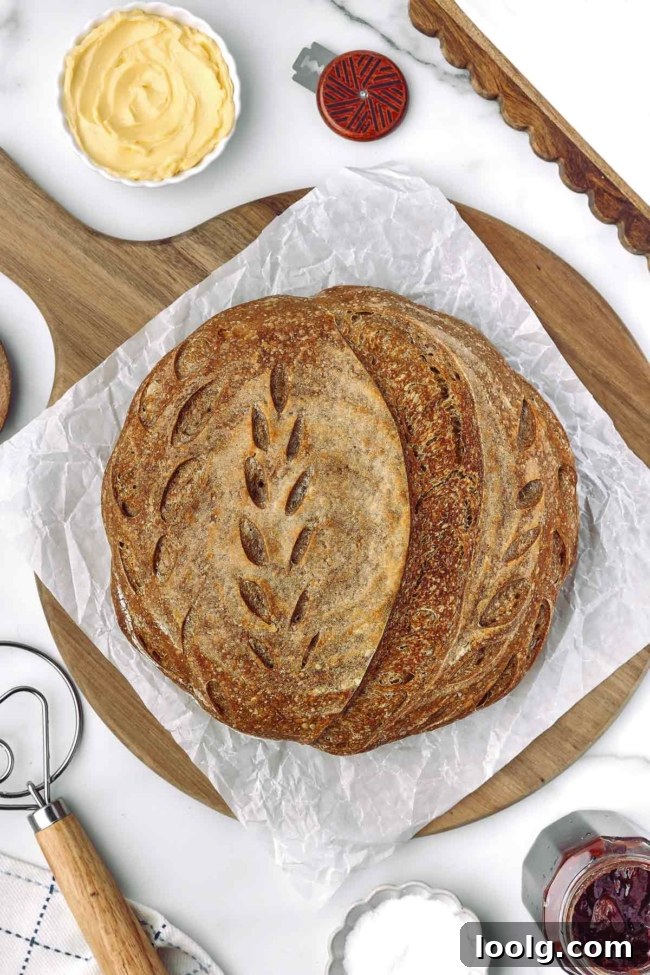 Whole wheat sourdough bread on parchment paper, surrounded by butter, jam, and baking tools on a wooden board.