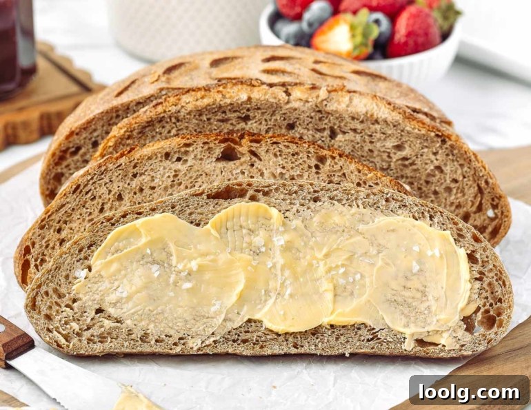 Sliced whole wheat sourdough bread spread with butter, showcasing its texture and crust.