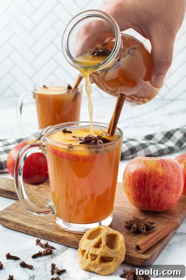 Shrunken Head Apple Cider: Spooky Halloween Drink Recipe 4 Warm spiced apple cider being poured into a glass with cinnamon sticks, star anise and fresh apples nearby.