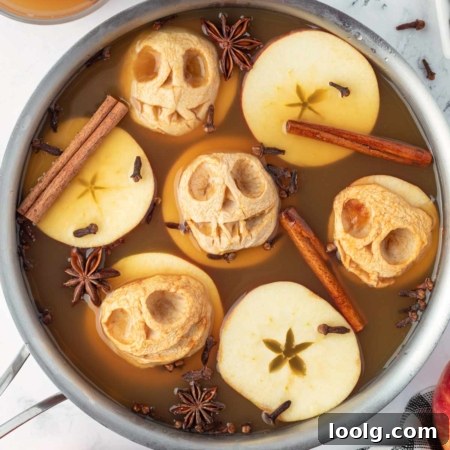 Shrunken Head Apple Cider: Spooky Halloween Drink Recipe 6 Spooky apple skulls float in spiced cider with cinnamon sticks and star anise, creating a festive autumn display.