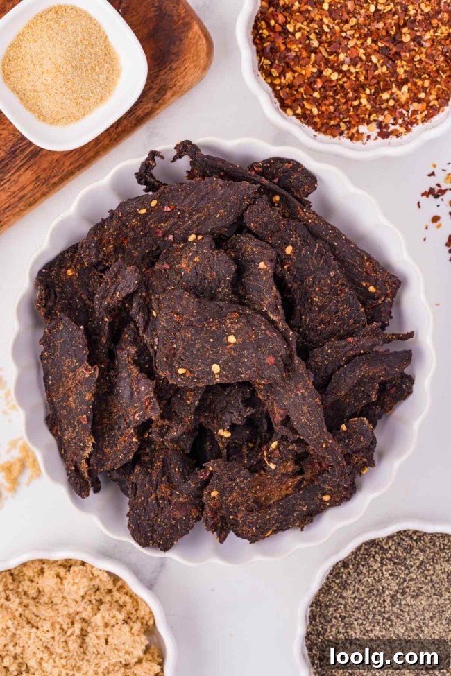 Homemade Smoky Venison Jerky Recipe 12 Savory venison jerky surrounded by various spices, including garlic powder, red pepper flakes, and black pepper.