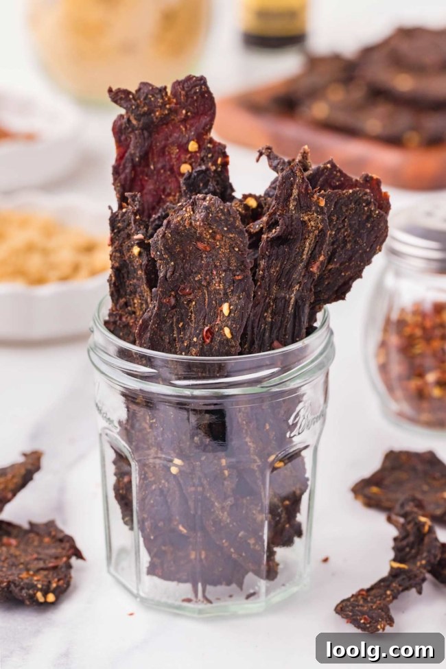 Homemade Smoky Venison Jerky Recipe 13 Venison jerky sticks are displayed in a glass jar, showcasing their rich color and seasoning.
