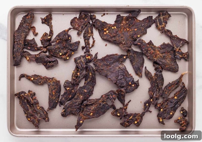 Homemade Smoky Venison Jerky Recipe 10 A tray of seasoned venison jerky pieces, showcasing a rich, dark color and a sprinkle of spices.